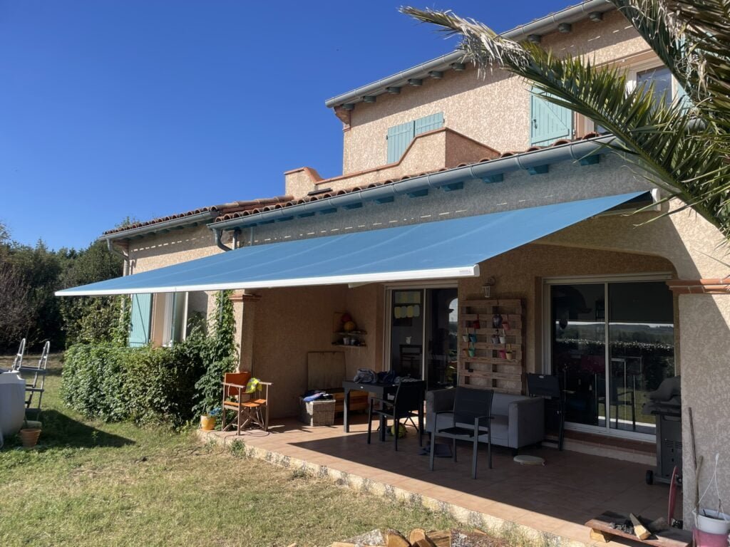 Grand store banne coffre motorisé bleu avec rétraction vent installé à Caraman (31460) par GPA Automatisme. Protection solaire optimale pour une grande terrasse ou vitrine commerciale