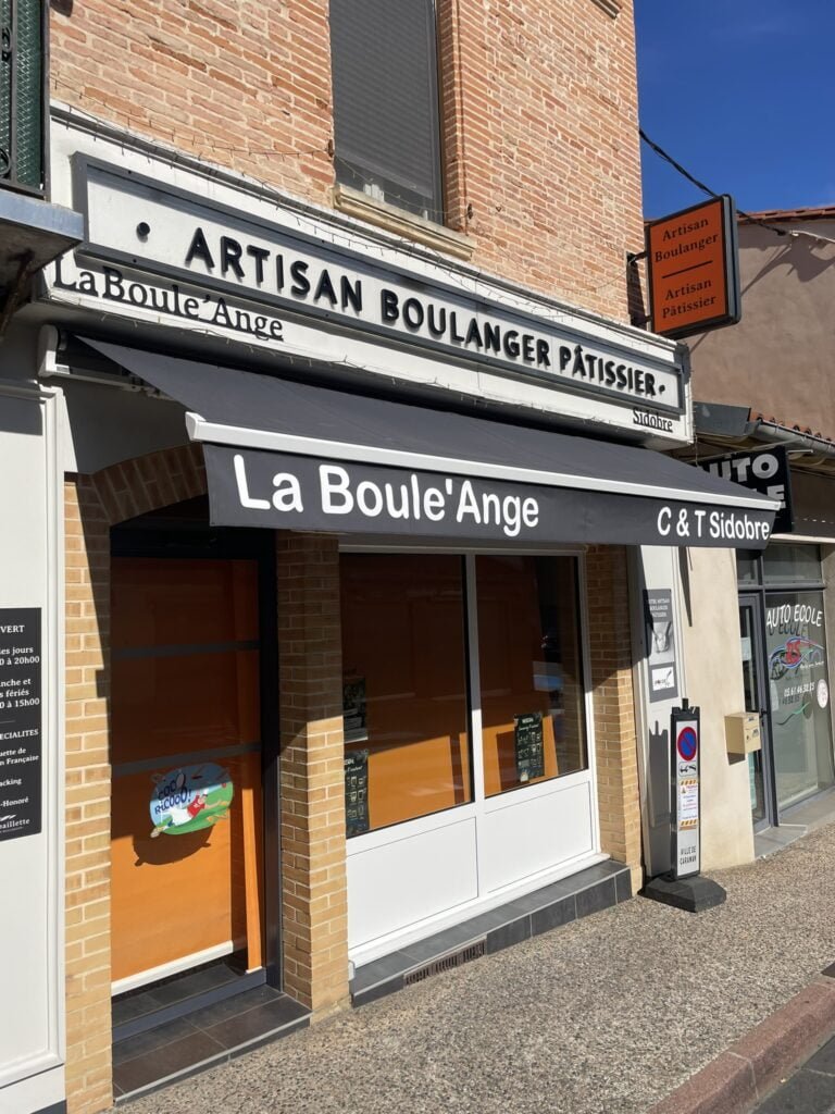 Store banne motorisé gris très grand et personnalisable installé à la boulangerie de Caraman (31460) par GPA Automatisme. Protection solaire et personnalisation pour une vitrine professionnelle attrayante