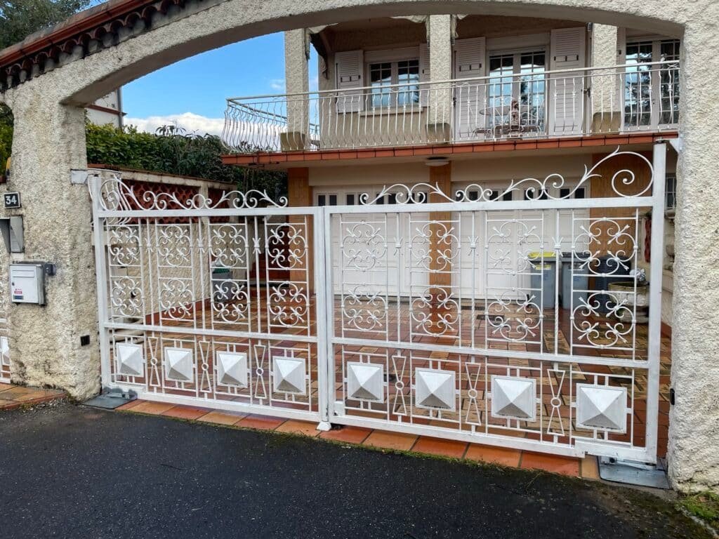 Portail battant blanc forgé motorisé installé à Ayguesvives (31450) par GPA Automatisme. Élégance et sécurité avec une motorisation performante adaptée aux particuliers et professionnels